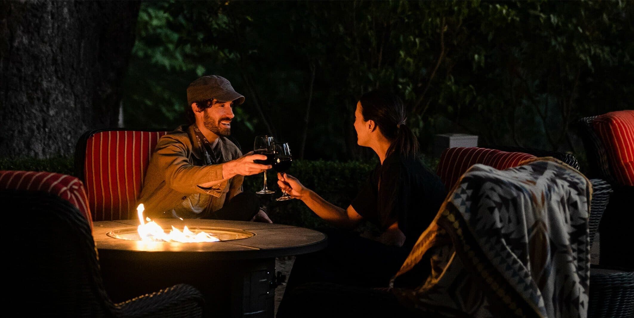 two people toasting wine over a fire pit outside