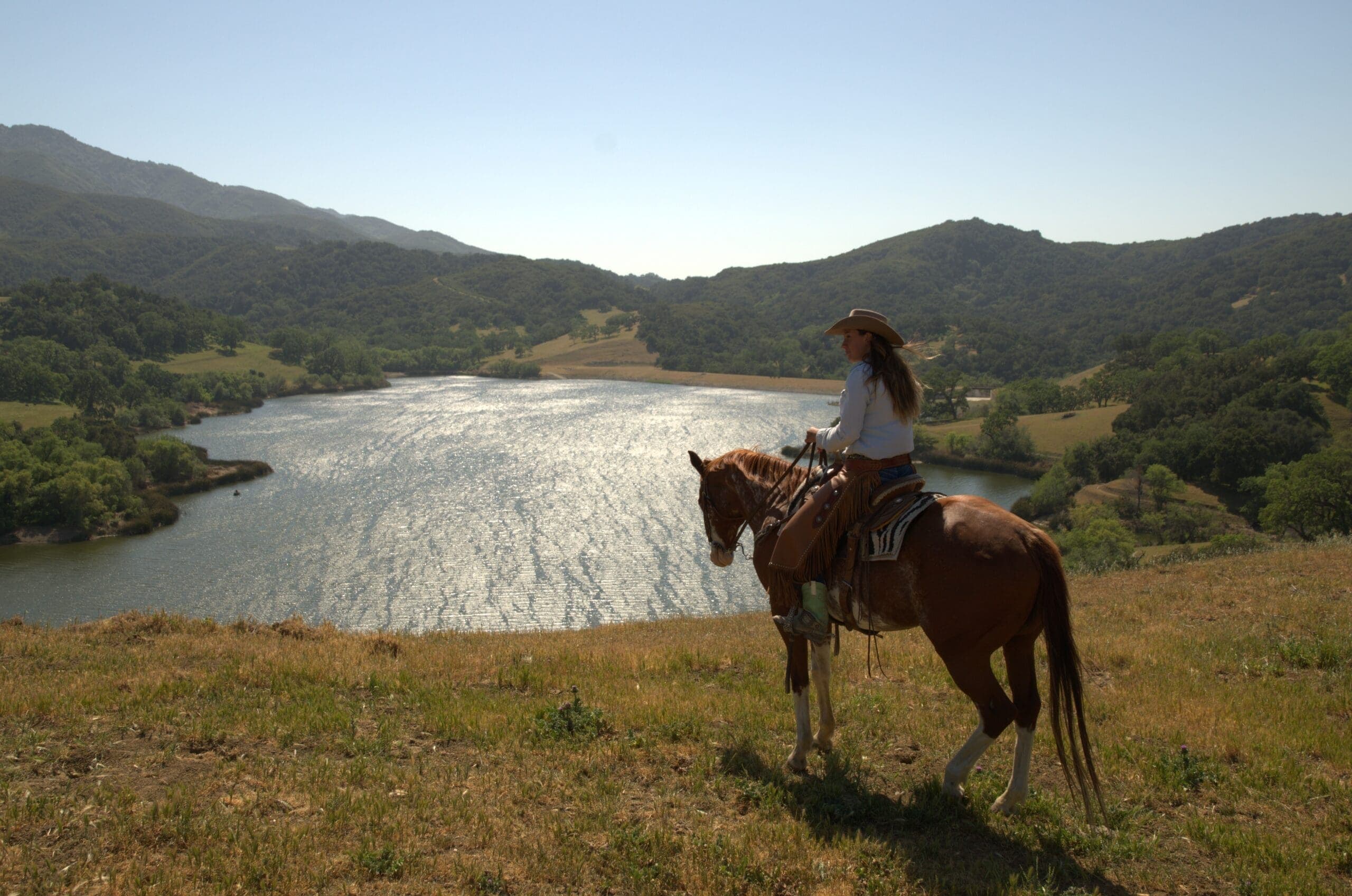 person riding horse on a grass hill overlooking the water