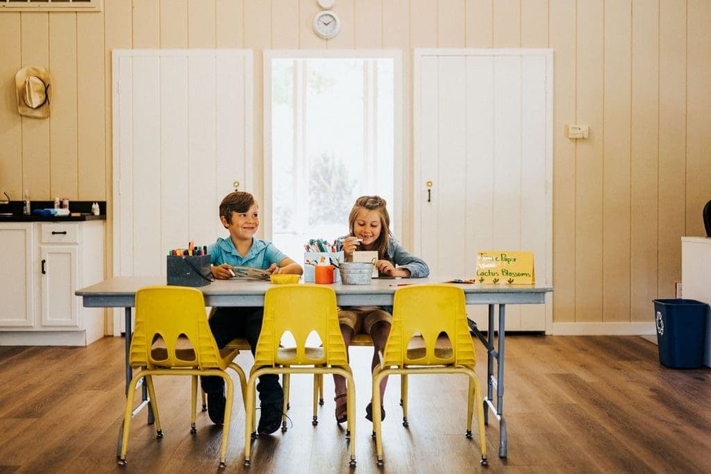 two kids sitting at a table with art supples