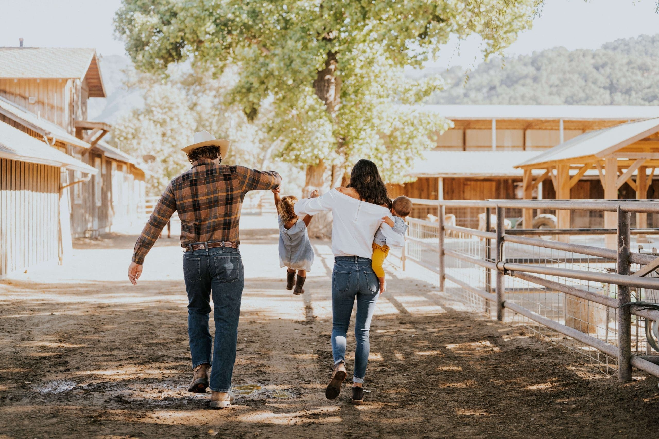 family walking along the dirt road beside the animals lifting their kids