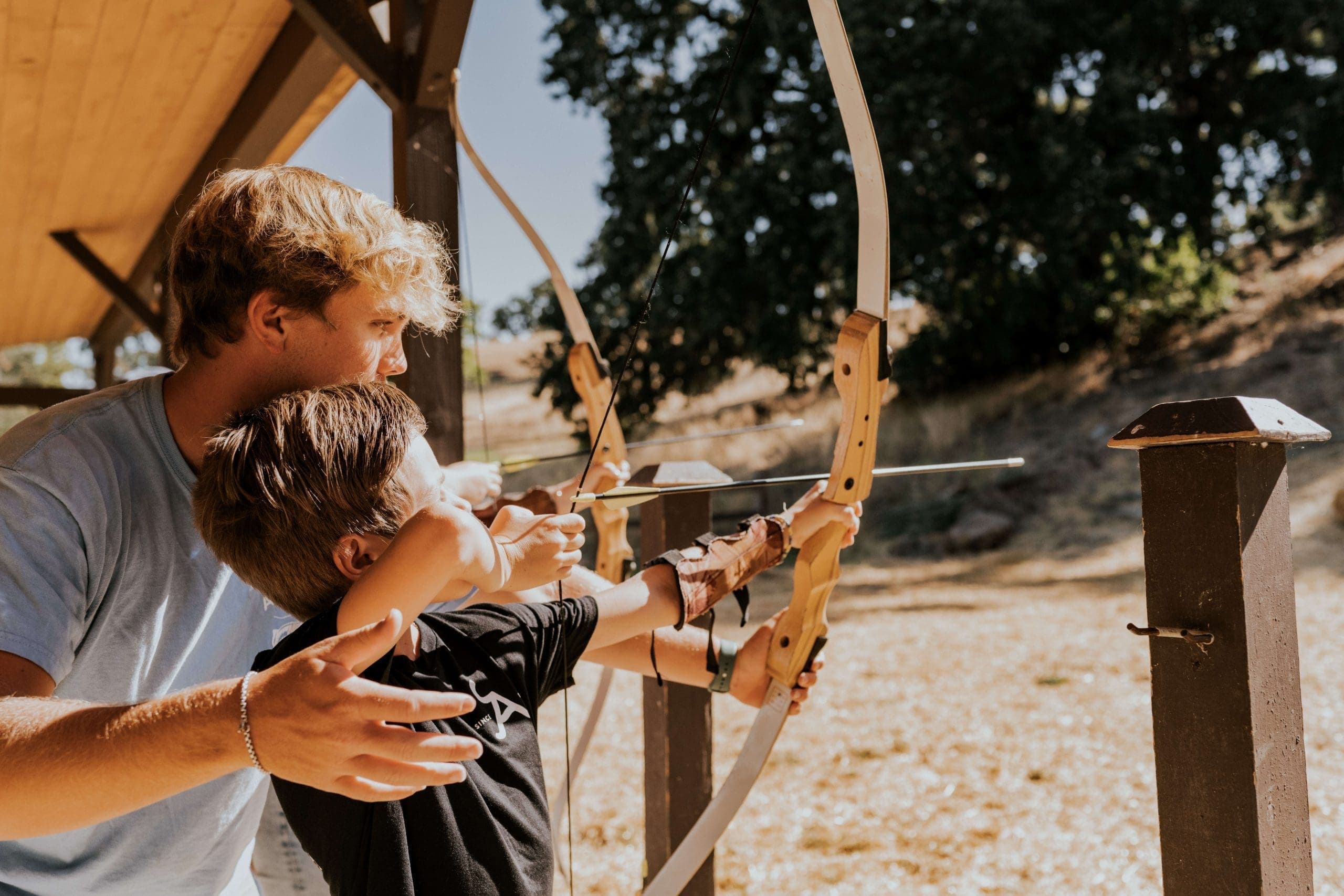 older person helping younger person point arrow and bow and target