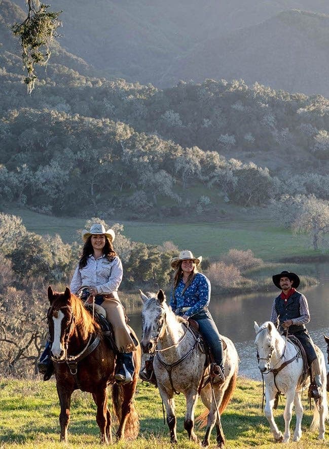 three people on horses smiling at the camera