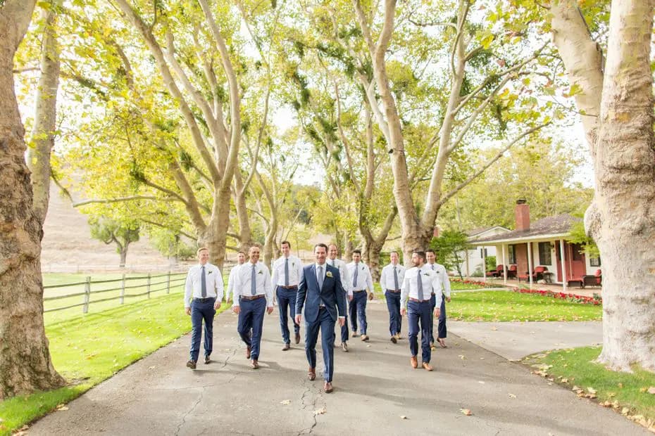 Groomsmen walking forwards in a tree lined lane at Alisal Ranch