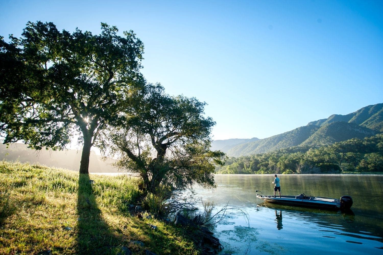 view of hills and person fishing on boat