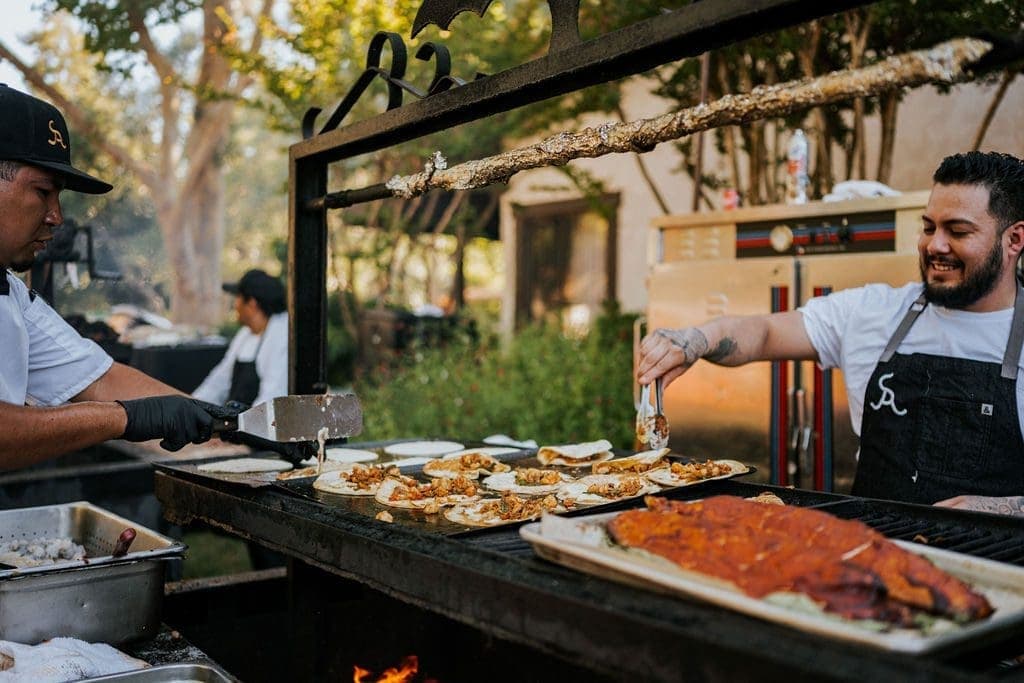 a person hold tongs over a barbecue full of tacos