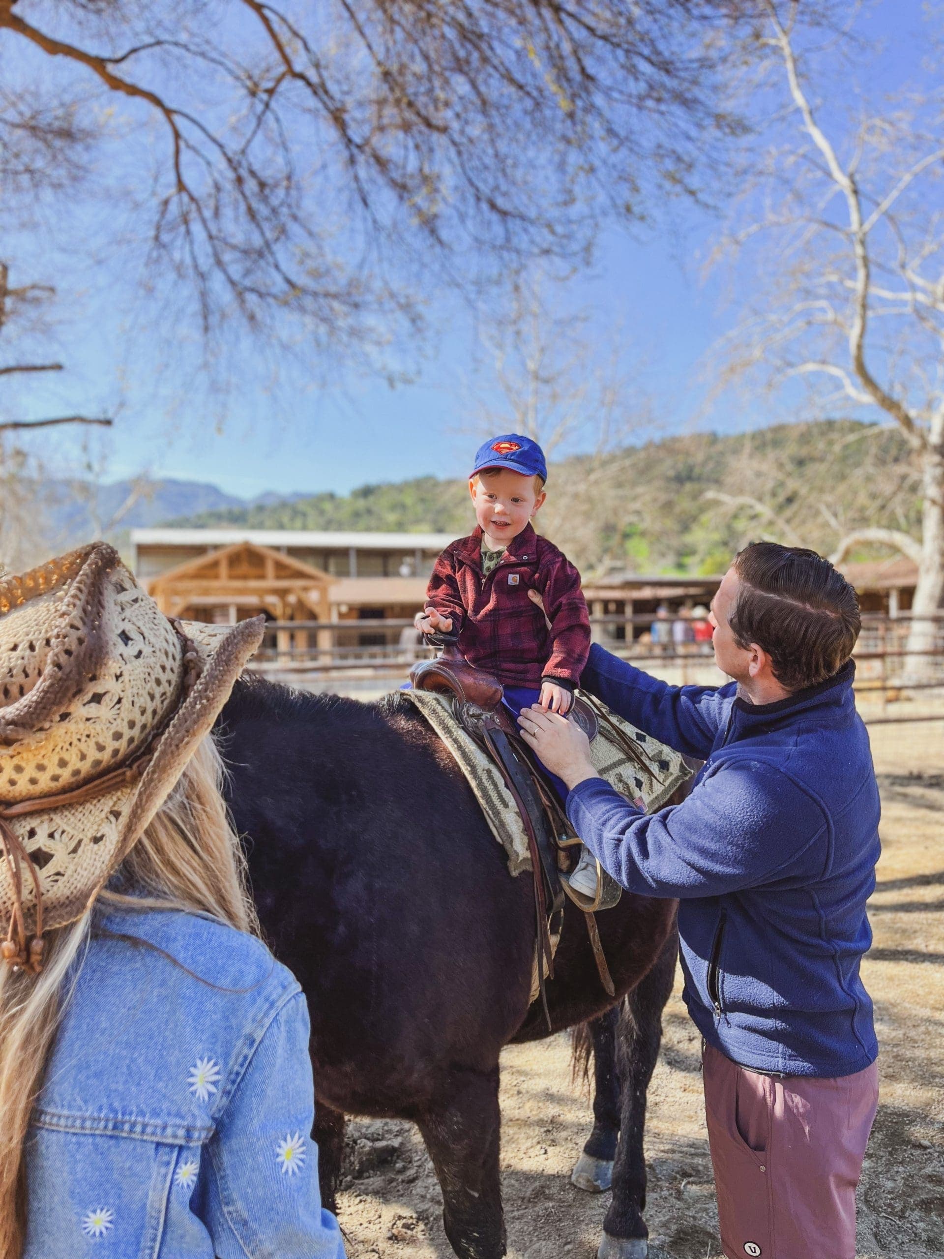 man supporting child as child sits on horse