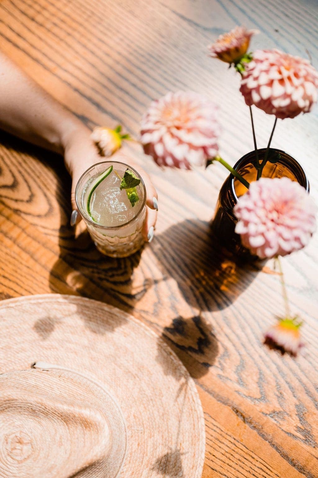 person holding a drink and pink flowers on a table
