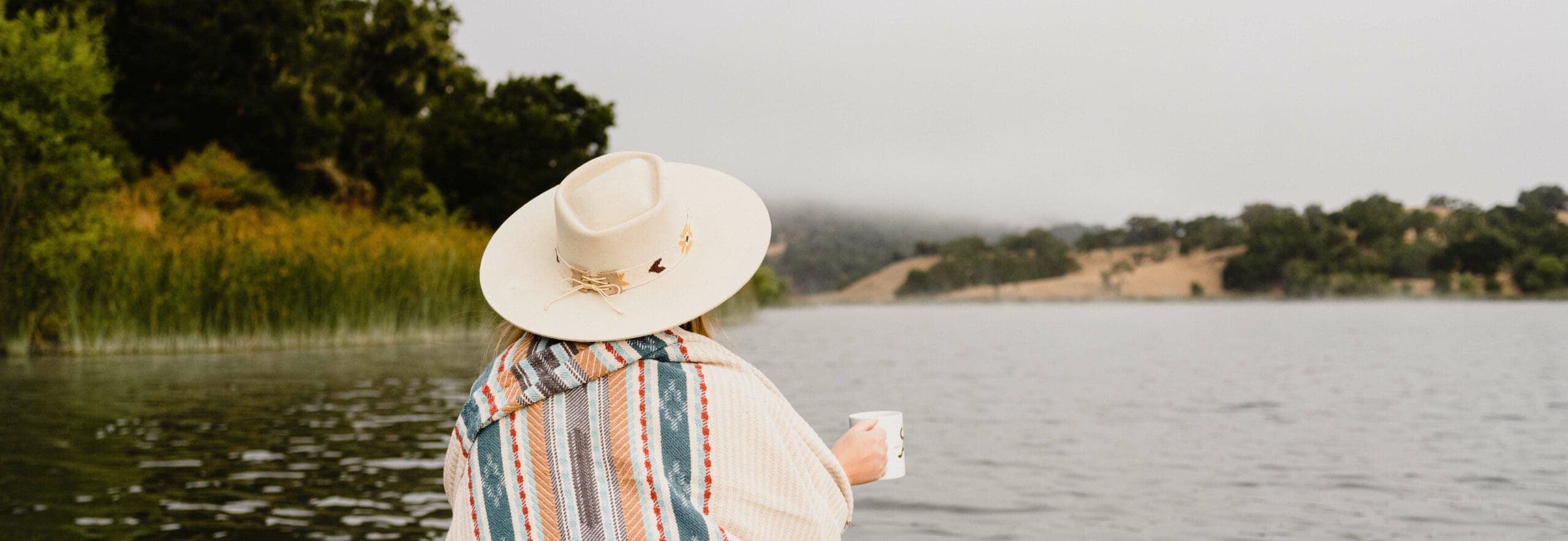 person holding a cup looking at the lake