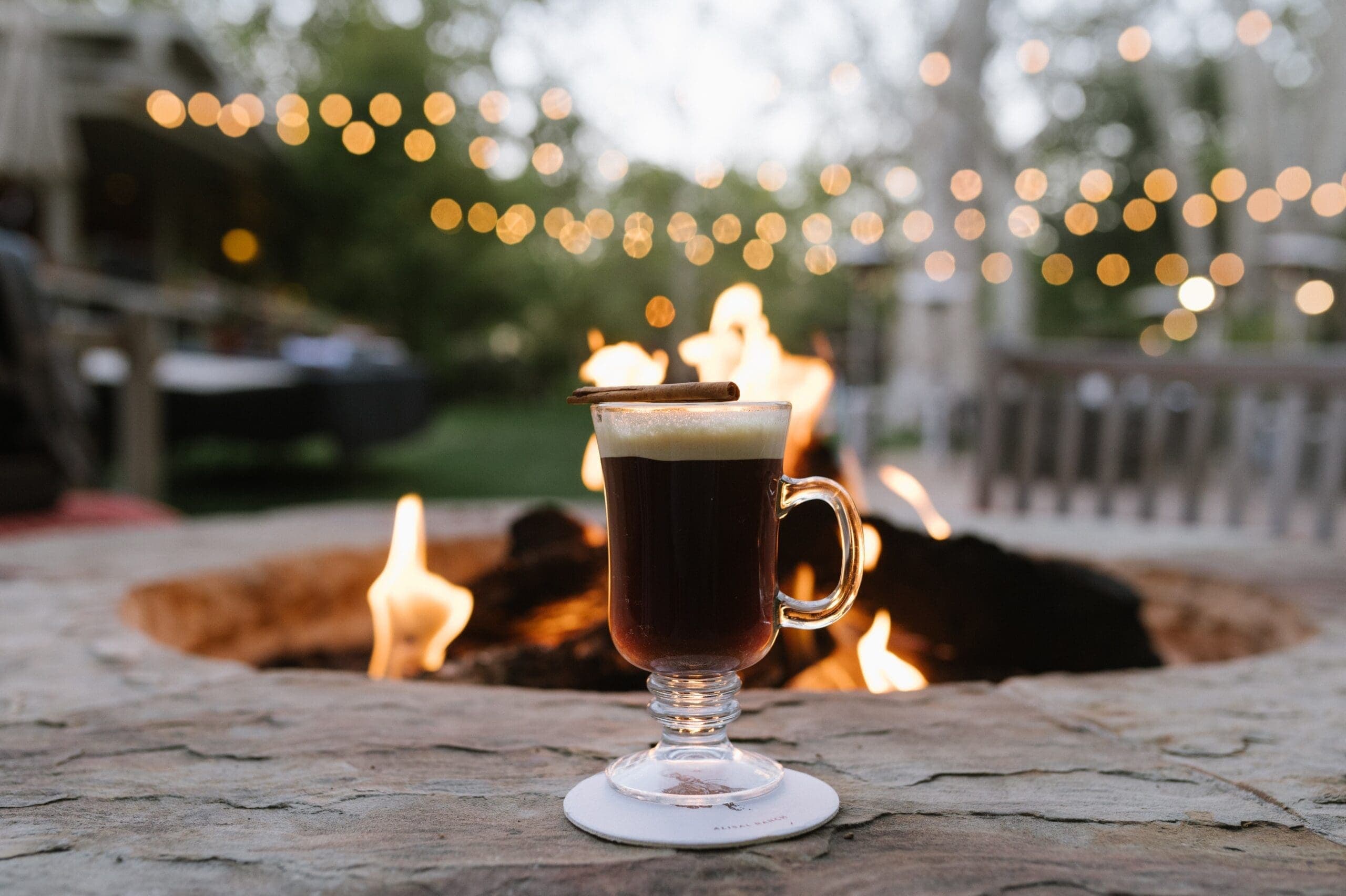 coffee in a class cup beside a lit fire pit