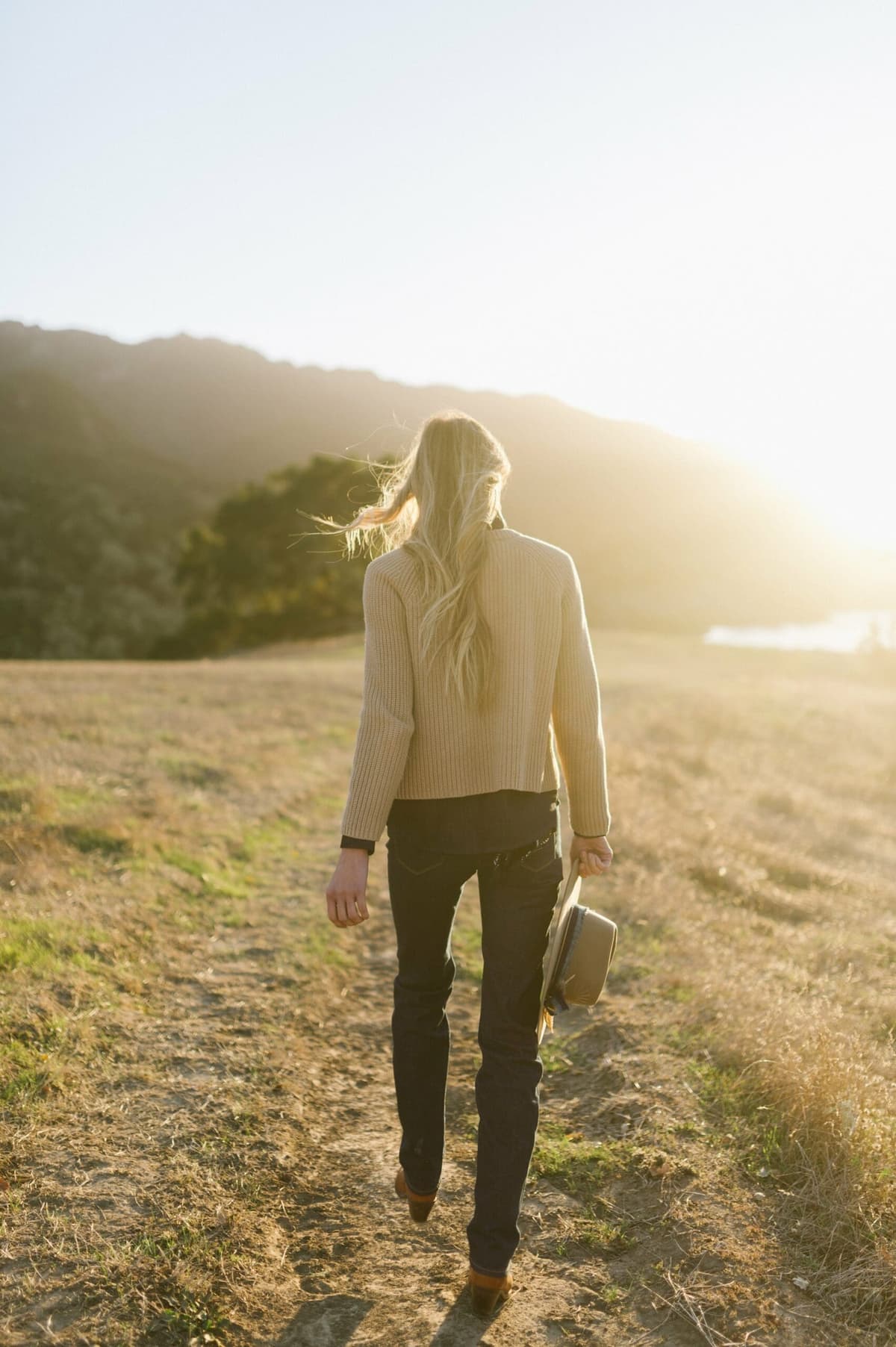 woman walking on grassing holding cowboy hat