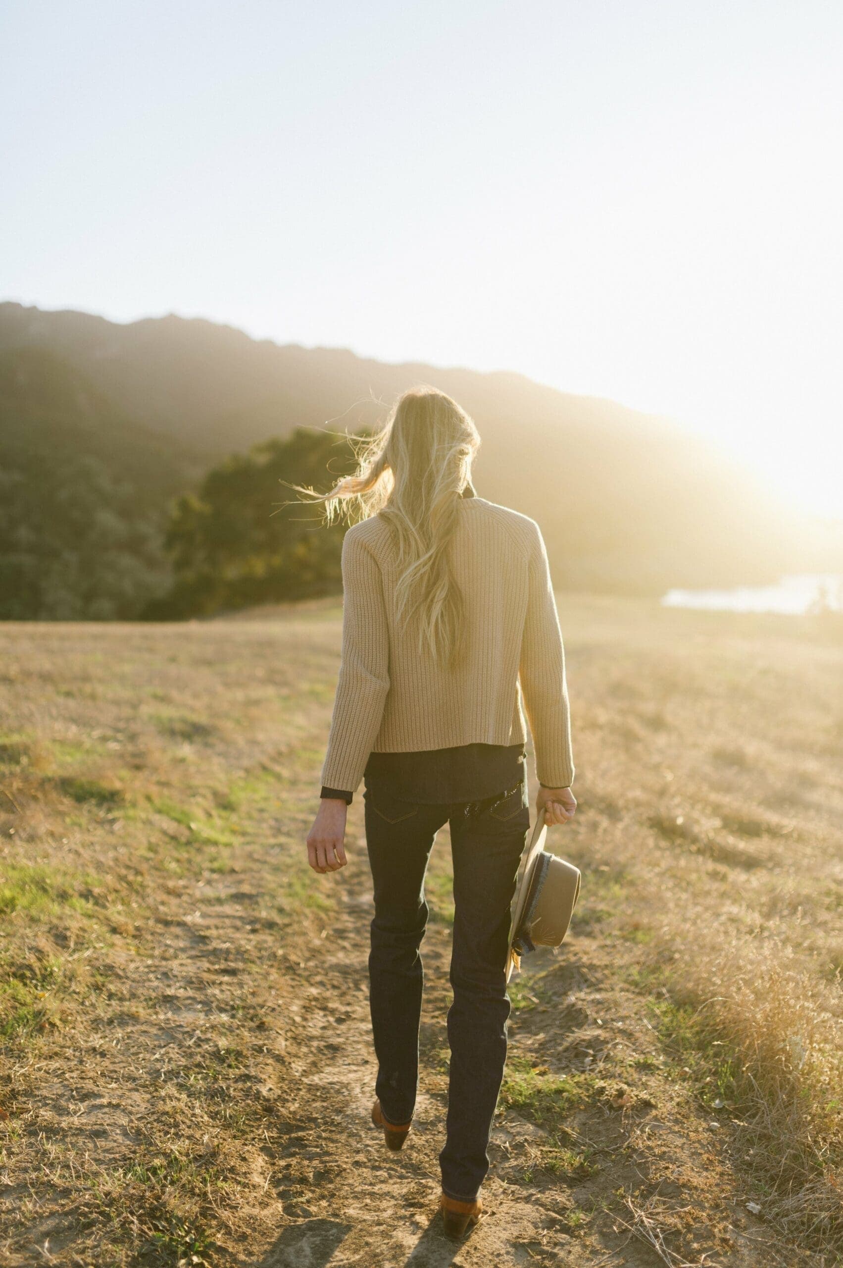 woman walking on grassing holding cowboy hat