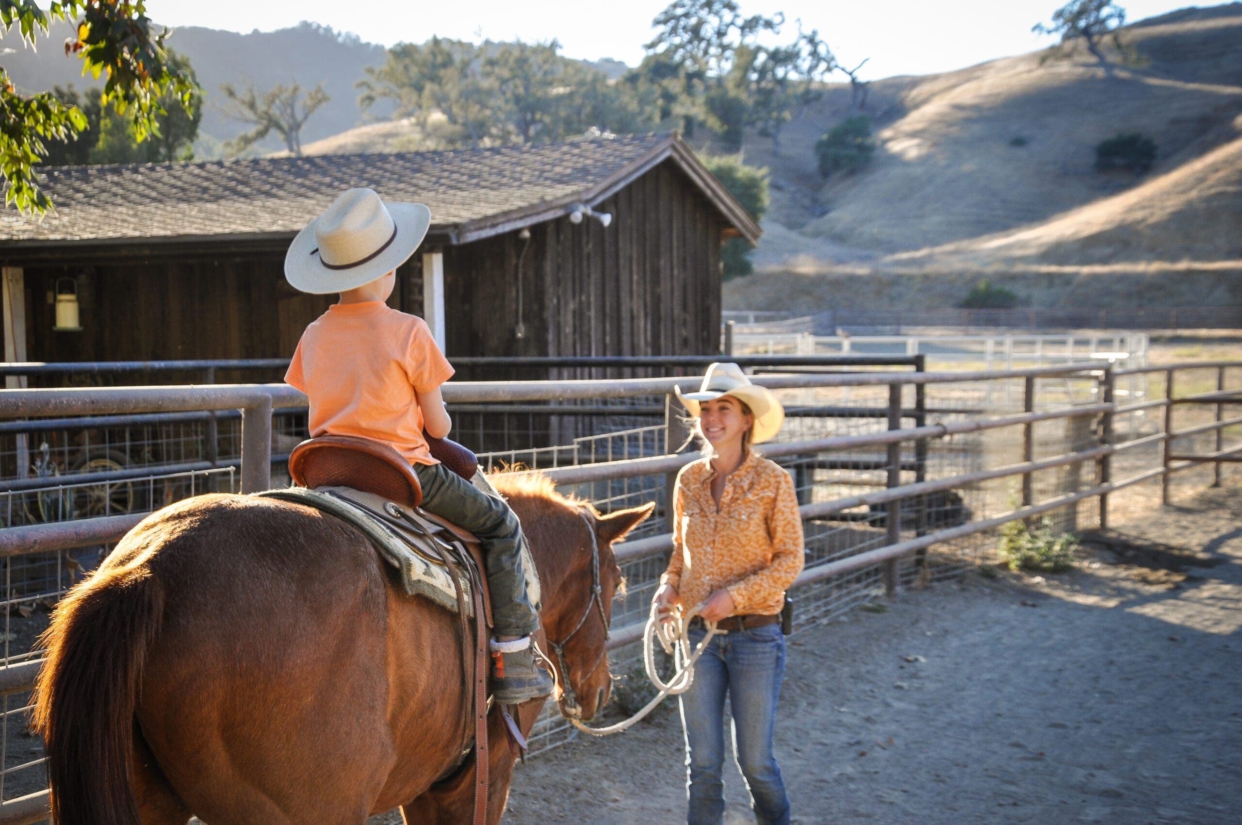 trainer holding reigns of horse with child seated on saddle