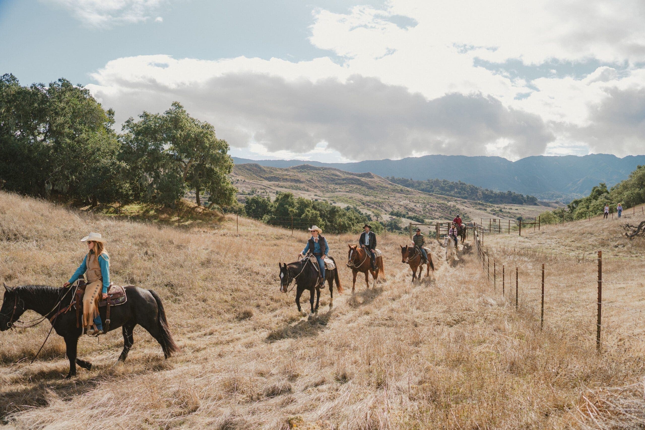 group of people riding horses inline on a dirt path