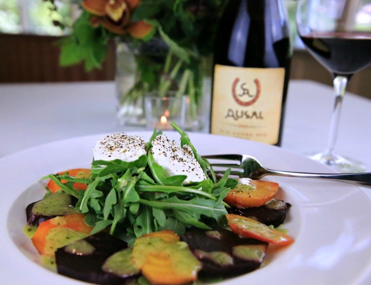 fresh tomato, arugula, burrata and balsamic vinegar salad on a plate beside Alisal red wine