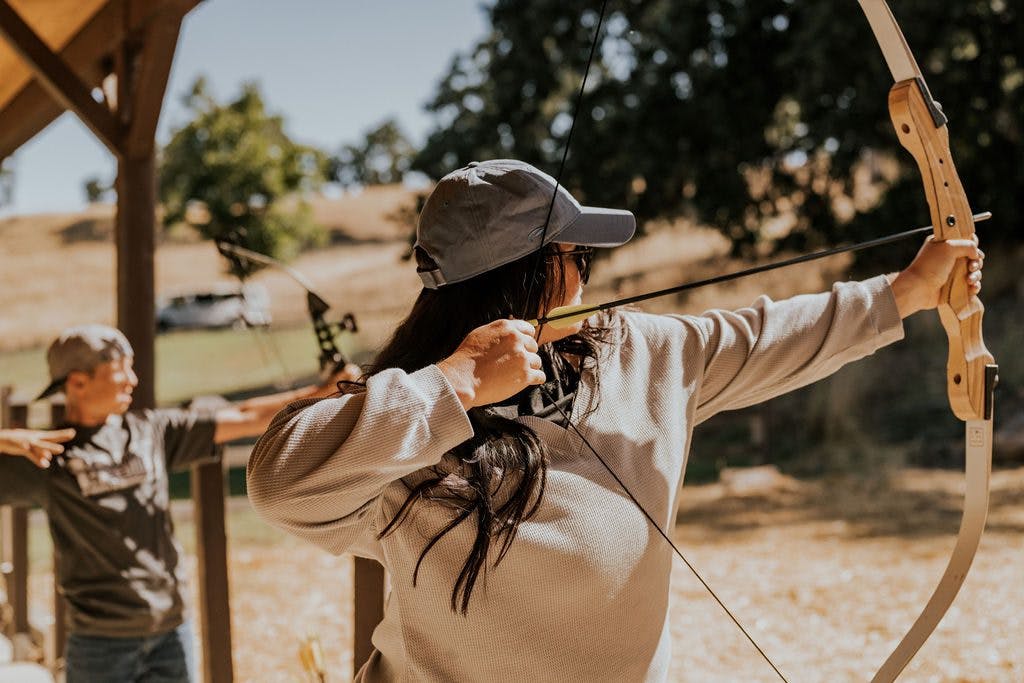 Woman pulling back bow at archery range at Alisal Ranch