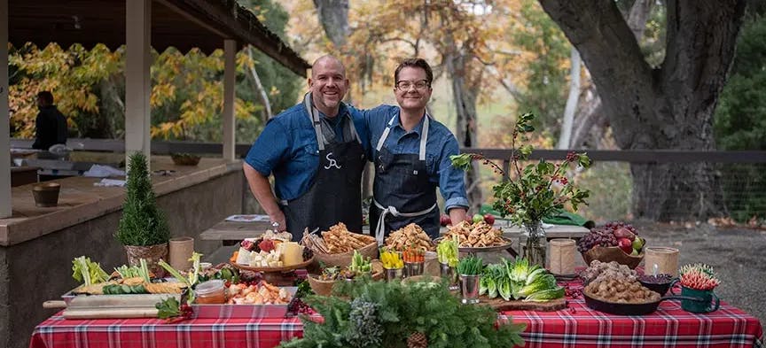 Nathan Turner and chef posing for the camera in front of a table full of holiday food