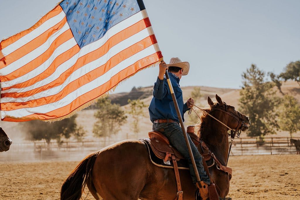 person riding horse holding American flag