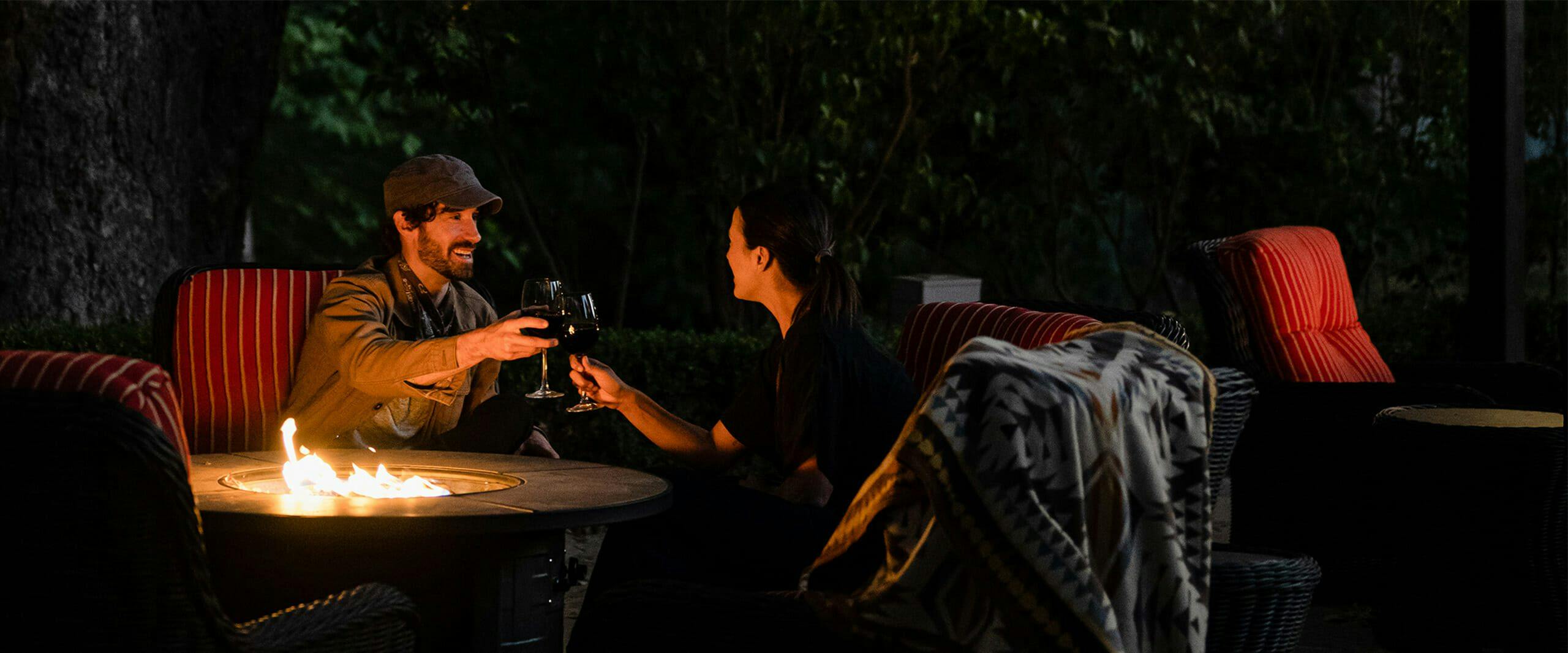 two people toasting wine over a fire pit outside