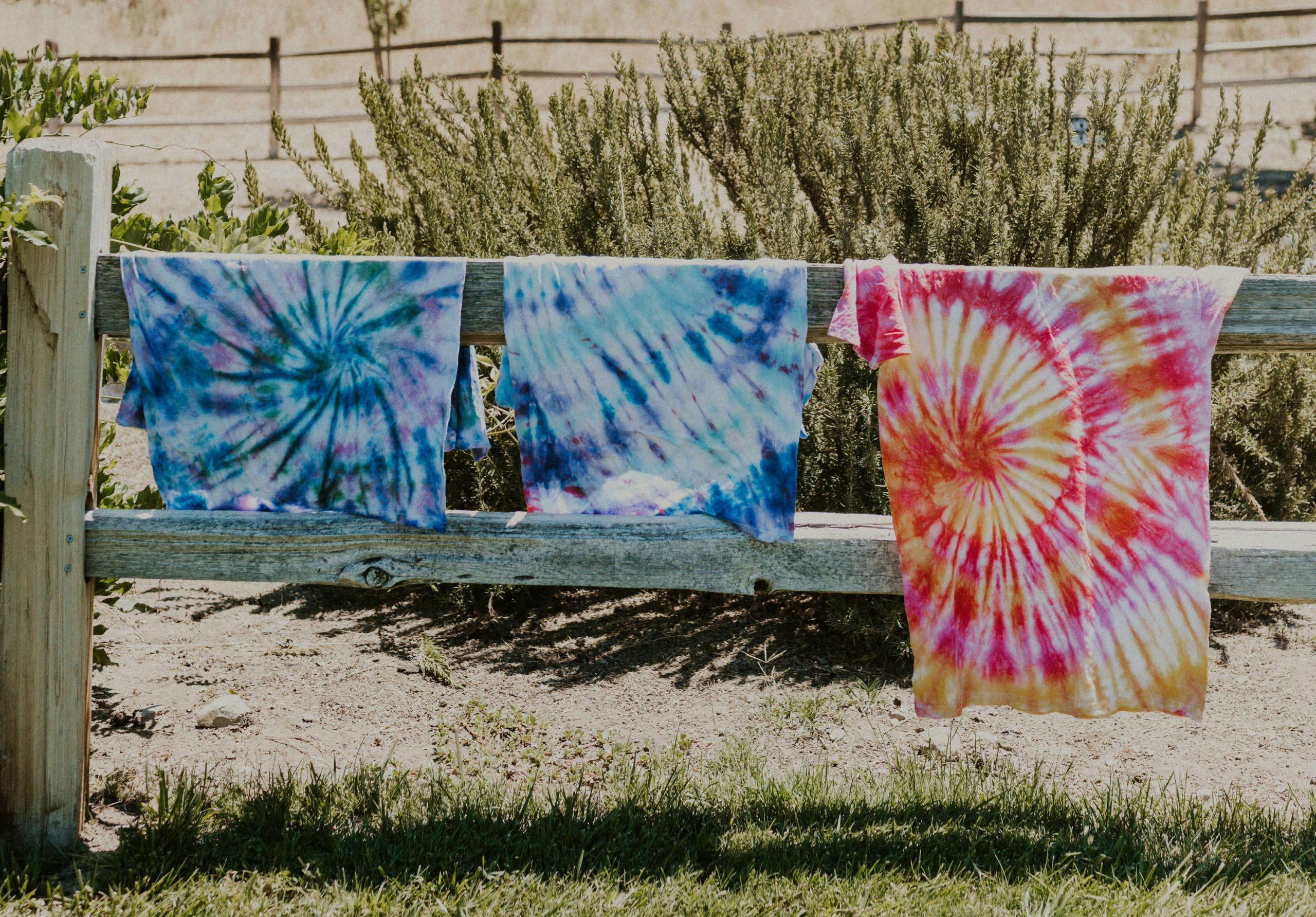 tie dyed t-shirts hanging on a fence