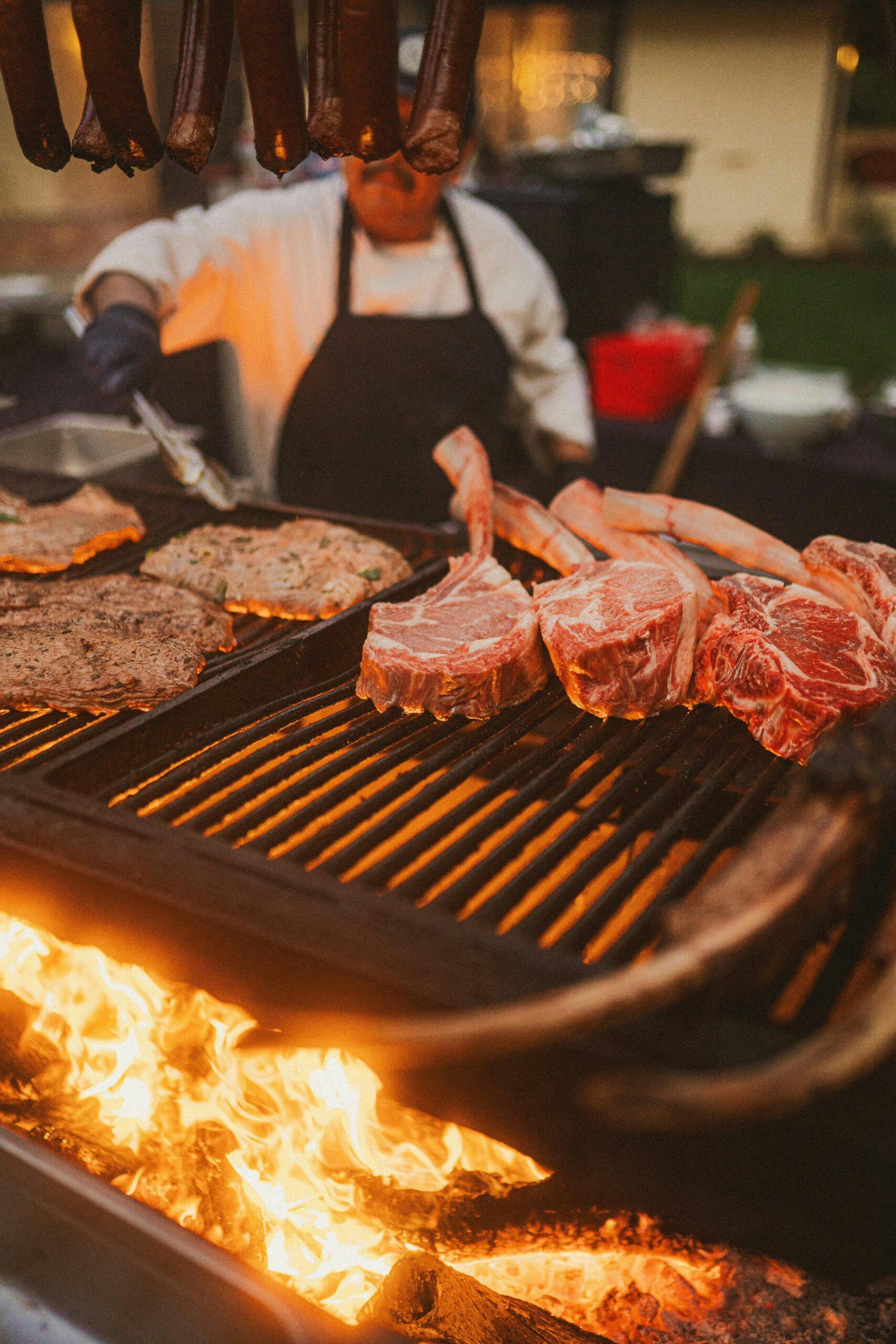 person barbecuing tomahawks and meat on a large grill