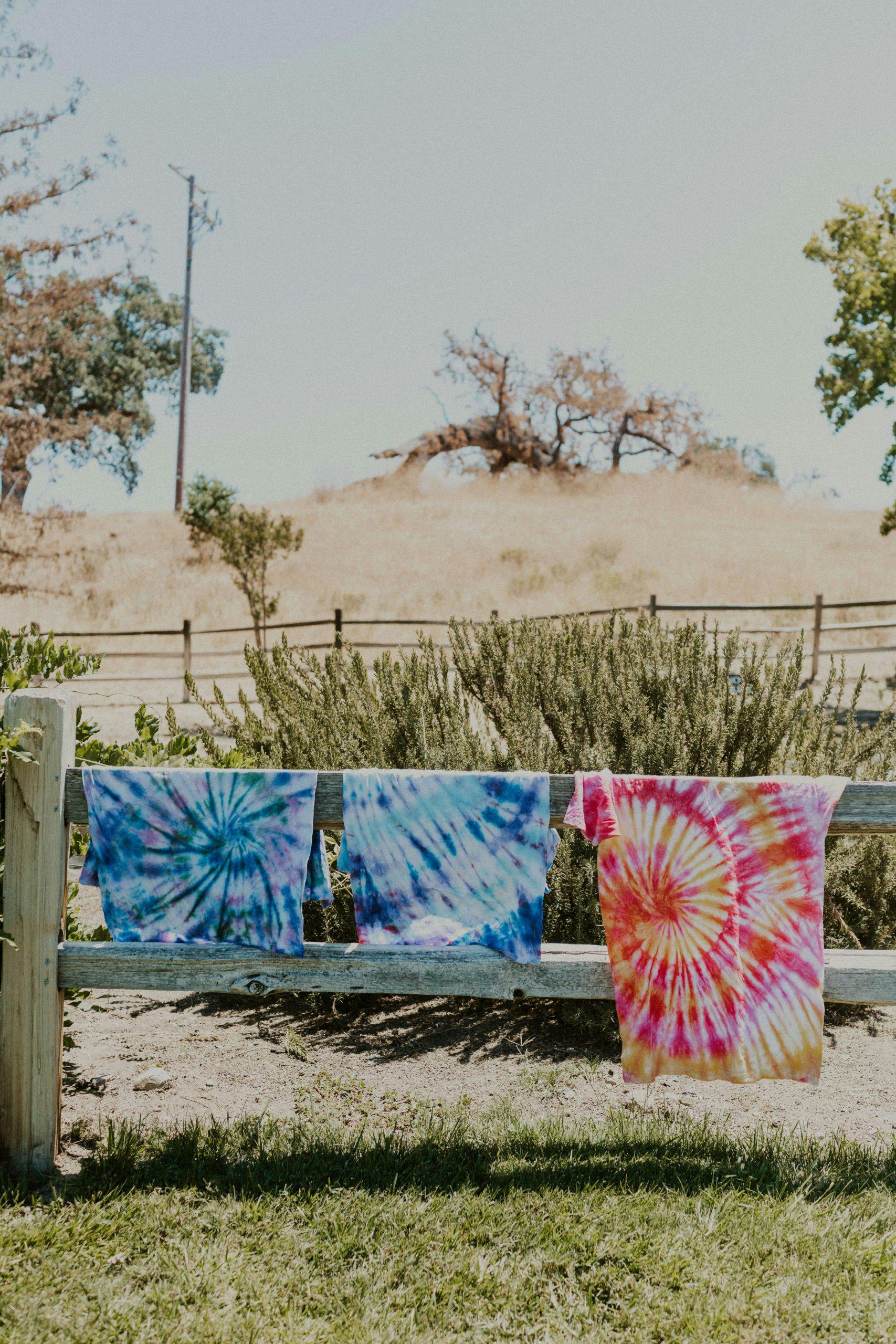 tie dyed shirts hanging on a fence