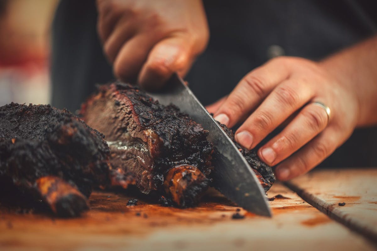 person cutting meat with a knife on a chopping board